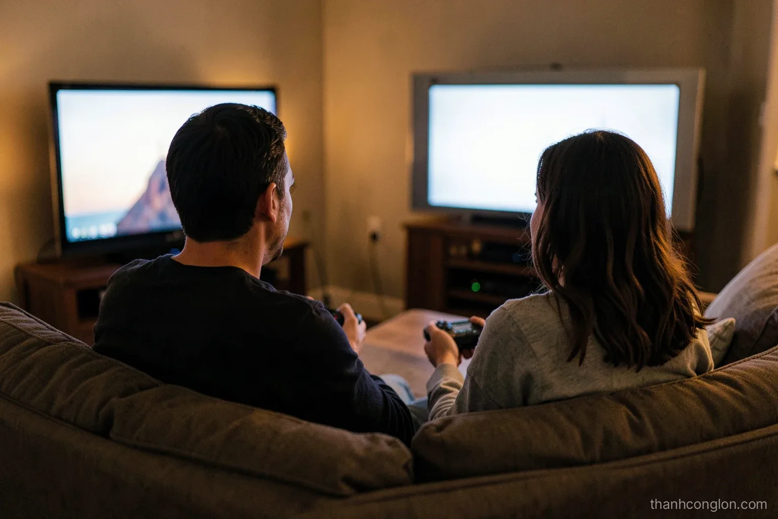 Over-the-shoulder view of two people seen from behind on a living room sofa holding small game controllers, the television glow lighting the room, evening warm tones