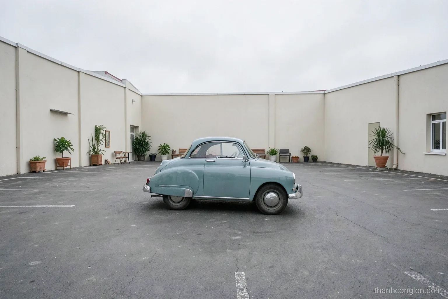 Small rounded vintage car parked alone in a vast empty parking lot under a pale overcast sky, photographed from far away, minimalist composition